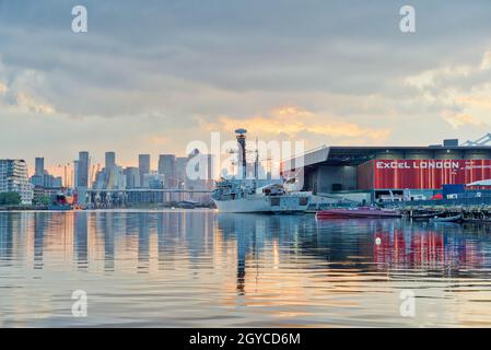 HMS Argyll F231 Kriegsschiff vor dem Victoria Dock vor Excel London, Blick auf den Sonnenuntergang über den Canary Wharf docklands London England Großbritannien Europa Stockfoto