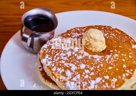 Klassischer Stapel von Pfannkuchen mit Puderzucker bestreut und mit Butterpuppe und Sirup gekrönt Stockfoto