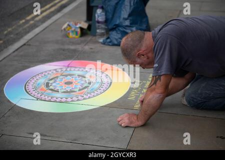 In Glastonbury zeichnet der Mensch in Regenbogenfarben ein Chakra in Kreide auf den Bürgersteig Stockfoto