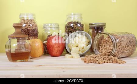 Bio-Honig mit Müsli, getrockneter Ananas und Äpfeln in rustikaler Küche Stockfoto