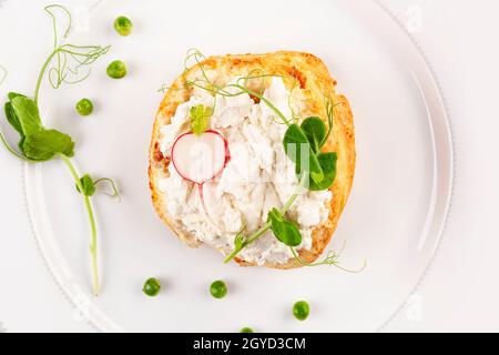 Leckeres Brot mit Frischkäse, Erbsen und Rettich auf weißem Teller von oben. Stockfoto