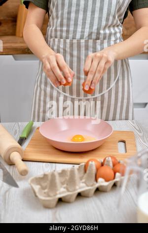 Frau bricht Eier in Schüssel. Hausfrau Kochen in der Küche zu Hause. Close-up Stockfoto