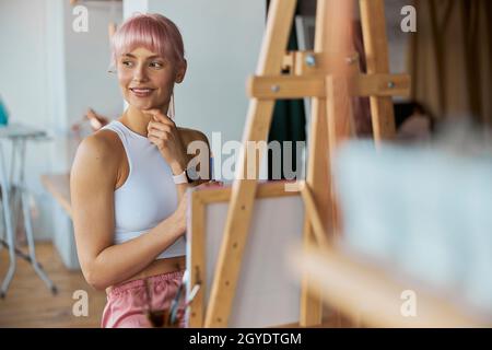 Elegante Künstlerin sitzt an der Staffelei mit weißer Leinwand auf zu Hause Stockfoto