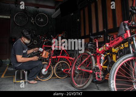 Bandung, Indonesien. Oktober 2021. Ein Mechaniker sah in der Werkstatt von Arusik Bikes in Bandung, wie er ein Batteriefach an einem Faltfahrrad installierte, das in ein Elektrofahrrad umgewandelt wird. Die Standard-Fahrrad-Innovation, die mit Strom modifiziert wird, basiert auf einem zusätzlichen Dynamo am Rad mit einem „Pedal Assist“- und „Gas-Gaspedal“-System, das bis zu 70 Kilometer hält. Die Custom-Akku-Power 'Arusik Bike' reicht von 250 bis 300 Watt bei einer Akkuladezeit von 4 Stunden von Null bis voll. Kredit: SOPA Images Limited/Alamy Live Nachrichten Stockfoto