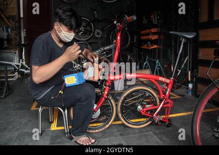 Bandung, Indonesien. Oktober 2021. Ein Mechaniker sah in der Werkstatt von Arusik Bikes in Bandung, wie er ein Batteriefach an einem Faltfahrrad installierte, das in ein Elektrofahrrad umgewandelt wird. Die Standard-Fahrrad-Innovation, die mit Strom modifiziert wird, basiert auf einem zusätzlichen Dynamo am Rad mit einem „Pedal Assist“- und „Gas-Gaspedal“-System, das bis zu 70 Kilometer hält. Die Custom-Akku-Power 'Arusik Bike' reicht von 250 bis 300 Watt bei einer Akkuladezeit von 4 Stunden von Null bis voll. Kredit: SOPA Images Limited/Alamy Live Nachrichten Stockfoto