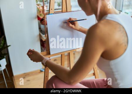 Künstlerin zeichnet Bild auf weißem Papier mit Graphitstift an HolzStaffelei im Lichtstudio Stockfoto