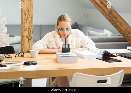 Junge Geschäftsfrau in kuscheligem warmen Bademantel, die in der Weihnachtszeit im Winter fernab vom Wohnzimmer arbeitet. Remote-Arbeit von zu Hause aus Stockfoto