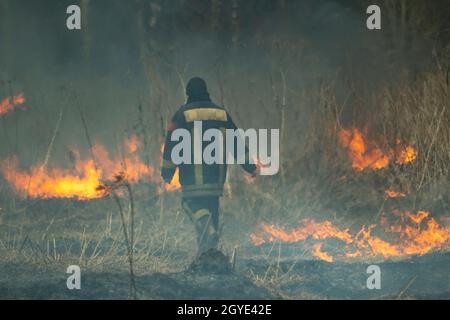 Ein Feuerwehrmann löscht ein Feuer in der Natur. Trockenes Gras brennt. Der Retter bekämpft das Feuer. Brände in Russland. Trockene Sommer sind gefährlich. Stockfoto