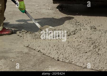 Den Mörtel mit einer Schaufel von der Straße reinigen. Beseitigung der Straße von verschüttetem Zement. Eine Schaufel in den Händen eines Arbeiters. Stockfoto