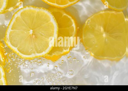 Zitronenscheiben in Wasser auf weißem Hintergrund. Nahaufnahme der Zitrone in Flüssigkeit mit Blasen. Scheiben von gelber, reifer Zitrone in Wasser. Makrobild von Früchten in wa Stockfoto