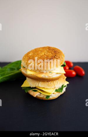 Leckerer Hamburger mit Tomaten, Cutlet, Brunnenkresse und Zwiebeln auf schwarzem Schiefer, im Hintergrund Salat und Kirschtomaten. Leerzeichen für Text Stockfoto