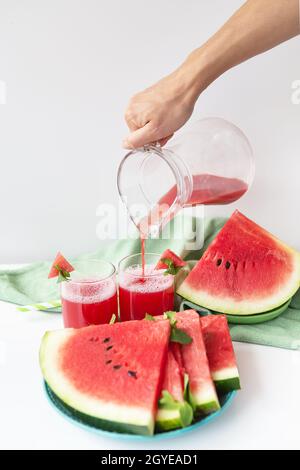 Das Mädchen gießt aus einem Krug frisch gepressten Saft aus frischer Wassermelone, einen gesunden Smoothie aus Wassermelone und Minzblättern Stockfoto
