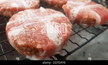 Rohe Fleischschnitzel, die in Speck eingewickelt sind, werden auf dem Grillrost gegarten. Der Küchenchef bereitet die gegrillten Burger-Patties zu. Zutaten für die Herstellung eines Hamburgers. Fleisch Stockfoto