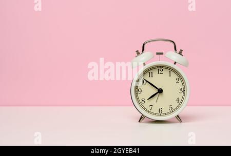 Weißer Metallwecker auf einem weißen Tisch, zehn bis acht Uhr morgens, Kopierplatz Stockfoto