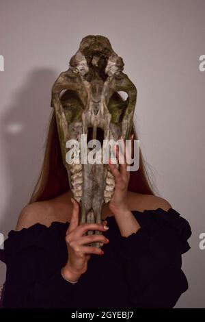 Weibchen hält eine Maske in Form eines Dinosaurierschädels Stockfoto