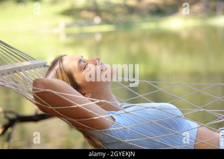 Profil einer Frau, die auf einer Hängematte liegt und sich neben einem See im Berg entspannt Stockfoto