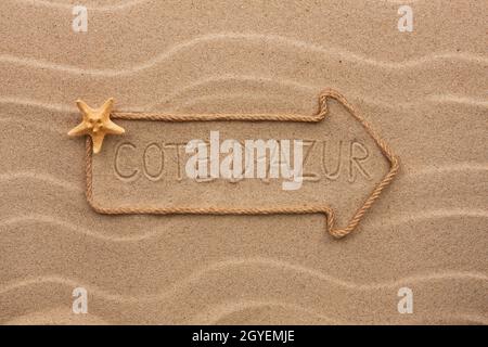 Pfeil aus Seil und Seestern mit dem Wort Côte d ' Azur auf dem Sand, als Hintergrund Stockfoto