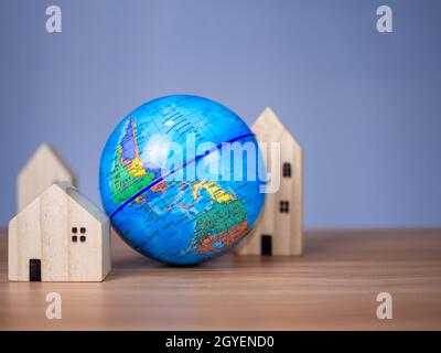 Ein Holzmodellhaus befindet sich neben einem nachgebildeten Globus. Platziert auf einem Holztisch mit hellgrauem Hintergrund. Save World Konzept Stockfoto