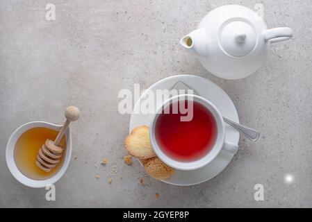 Teetasse und Teekocher mit Obst, Kräuter mit Honig auf grauem Tischhintergrund Stockfoto