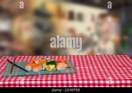 Tischplatte auf Sushi Hintergrund. Nahaufnahme von verschiedenen Arten von Sushi und Essstäbchen auf grüner Bambus matte serviert auf einem Rot karierte Tischdecke gegen abstr Stockfoto