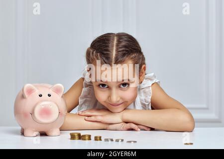 Kleines Mädchen mit Sparschwein und Stapel von Münzen zu Hause Stockfoto