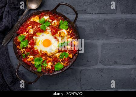 Shakshouka - Gericht aus Eiern pochiert in einer Sauce aus Tomaten, Olivenöl, Paprika, Zwiebeln und Knoblauch auf schwarzem Hintergrund Stockfoto