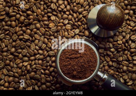 Halter mit frisch gemahlenem Kaffee liegt auf einem Hintergrund aus frisch gerösteten Kaffeebohnen, mit Kopierraum Stockfoto