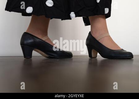 Beine einer Frau, die Flamenco mit schwarzen Kleidern auf Holzboden und weißem Hintergrund tanzt Stockfoto