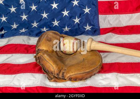 Die Nahaufnahme eines alten Baseballs und der Handschuh gegen die amerikanische Flagge zeigen eine der beliebtesten Sportarten des Landes. Stockfoto