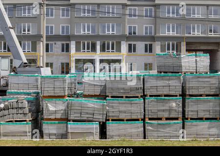 Auf der Baustelle befinden sich viele neue graue Pflasterplatten auf Kunststoff-überdachten Paletten. Pflaster von Fußgängerwegen auf einer Stadtstraße. Ukraine, Ki Stockfoto