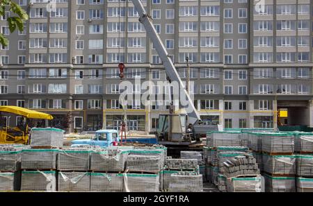 Auf der Baustelle befinden sich viele neue graue Pflasterplatten auf kunststoffgedeckten Paletten. Pflaster von Fußgängerwegen auf einer Stadtstraße. Vordergrund. Rep Stockfoto