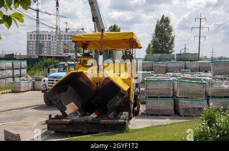 Auf der Baustelle ist ein Asphaltfertiger geparkt. Straßenbaugeräte stehen in einem Lager an der Straße. Schwere Straßenbau und Straße Stockfoto