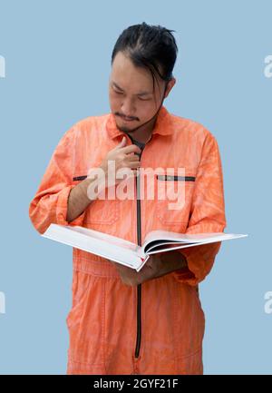 Der Hauptmechaniker in der orangen Uniform, der das große Buch hält. Stellen Sie sich auf und lesen Sie das Wartungshandbuch sorgfältig durch. Porträt mit Studiolicht. Stockfoto