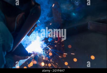 Schweißer schweißen Metall mit Argon-Lichtbogen-Schweißmaschine und hat Schweißfunken. Ein Mann trägt eine Schweißmaske. Sicherheit am Arbeitsplatz. Schweißmaschine arbeitet Stockfoto