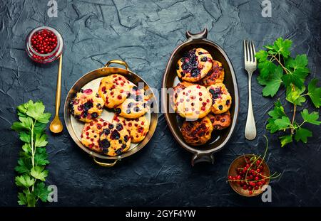 Appetitliche Hüttenkäse-Pfannkuchen oder Syrniki mit Sommerbeeren. Quark-Krapfen mit roten und schwarzen Johannisbeeren Stockfoto