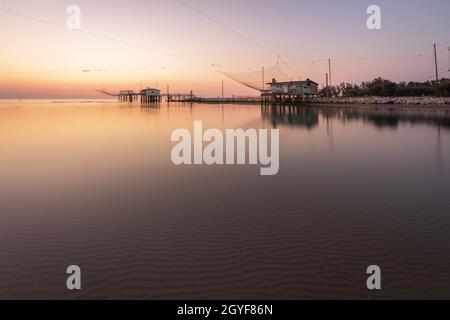 Landschaftsaufnahme von Fischerhütten am Fluss bei Sonnenaufgang mit typischer italienischer Fischmaschine, genannt 'trabucco', Lido di Dante, fiumi uniti Ravenna in der Nähe von Com Stockfoto