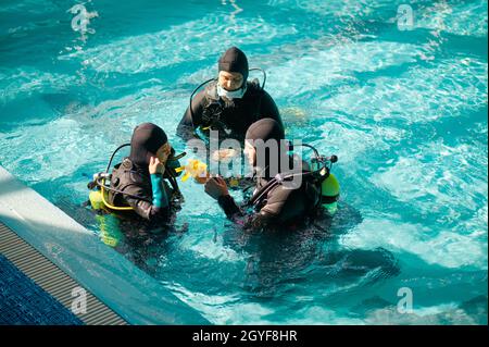 Tauchlehrer und zwei Taucher in den Aqualungs, Tauchkurs in der Tauchschule. Unterwasser-Schwimmen mit Tauchausrüstung, Hallenbad mit Innenbecken Stockfoto