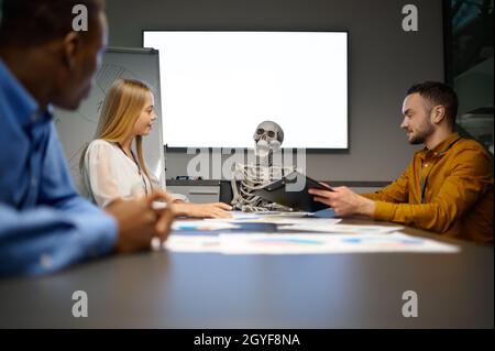 Team von Managern und Skelett, Konferenz im IT-Büro, Witz. Professionelle Teamarbeit und Planung, Brainstorming in der Gruppe und Unternehmensarbeit, Treffen von c Stockfoto