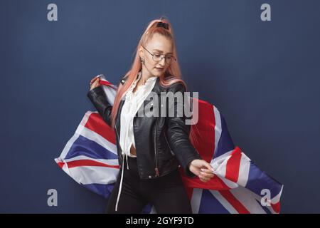 Junge Frau Expat in Brillen mit Großbritannien Flagge. Studioaufnahme. Hipster-Lehrerin in englischer Sprache. Fashionly gekleidete Frau mit rosa Haaren in bla Stockfoto