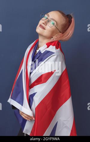 Junge Frau Expat in Brillen mit Großbritannien Flagge. Studioaufnahme. Hipster-Lehrerin in englischer Sprache. Fashionly gekleidete Frau mit rosa Haaren in bla Stockfoto