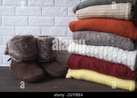 Ein Stapel warme Strickkleidung und Heimschuhe. Komfortable gemütliche Dinge für zu Hause. Herbst- und Winterkonzept. Stockfoto