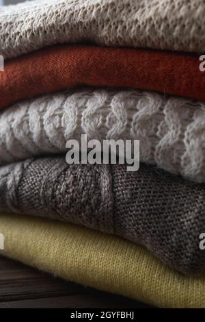 Kuschelige Pullover in Herbstfarben auf braunem Holzhintergrund. Verschiedene Strickmuster aus nächster Nähe. Stockfoto