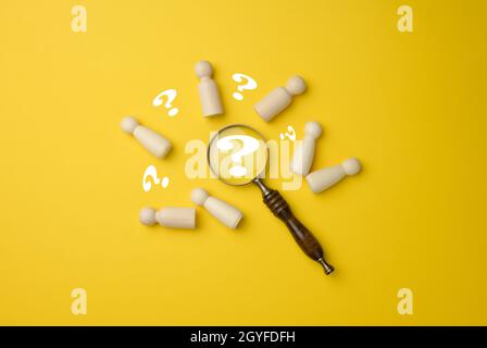 Holzmänner und eine Lupe auf gelbem Hintergrund. Rekrutierungskonzept, Suche nach talentierten und fähigen Mitarbeitern, Karriereentwicklung, Flat Lay Stockfoto