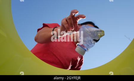 Recycling-Plastikflasche in der Perspektive von unten gesehen, aus dem Inneren des Eimers und kaukasische Frau, die eine oder mehrere hockte Plastikflaschen di wirft Stockfoto