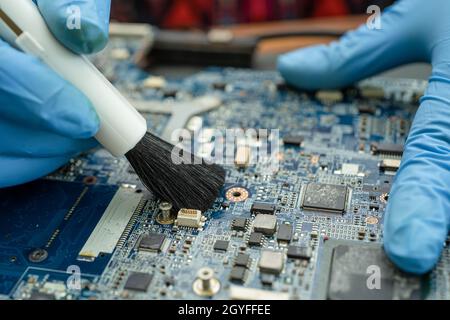 Der Techniker verwendet eine Bürste und eine Luftgebläse, um Staub im Leiterplattencomputer zu reinigen. Reparatur Upgrade und Wartung Technologie. Stockfoto