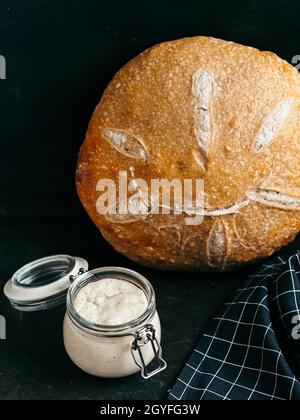 Sauerteig Vorspeise und Weizensauerteig Brot. Weizensauerteig Starter im Glas und leckere hausgemachte runde Sauerteig Brot auf schwarzem Hintergrund. Ho Stockfoto