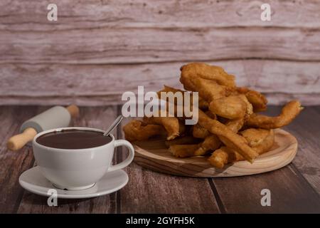 tasse heiße Schokolade mit frisch zubereiteten Churros auf Holzhintergrund typisch spanisches Frühstück an Feiertagen Stockfoto