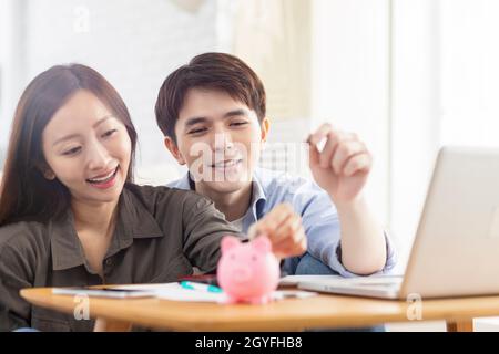 Glückliches Paar, das Münze in Sparschwein einsteckt.Haushalt zu Hause.Finanzierung der Familie. Stockfoto