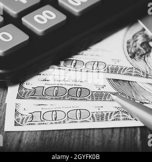 Dollar in 100-Dollar-Scheinen sind auf dem Tisch neben einem Rechner, einer Kreditkarte und einem Stift verteilt. Einhundert-Dollar-Scheine. US-Dollar. Stockfoto