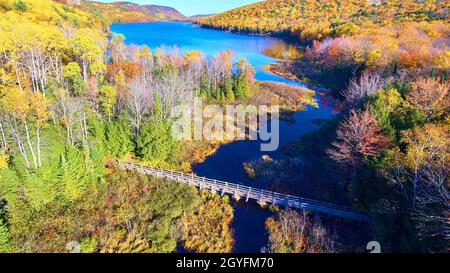 Wandern Brücke aus Holz über einen Fluss, der zu einem Riesen wie in den Bergen von einem Herbstwald umgeben führt Stockfoto